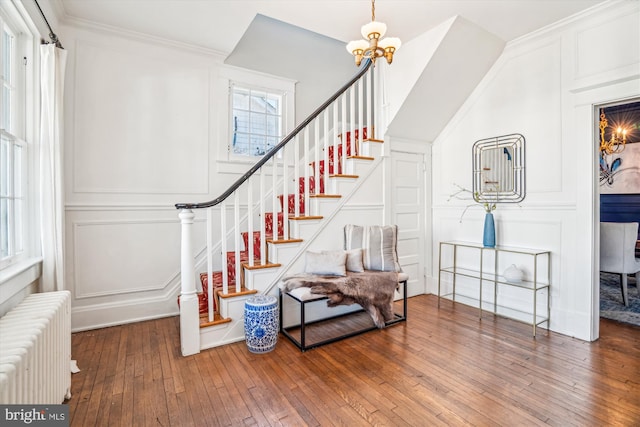 staircase with wood-type flooring, ornamental molding, radiator, and an inviting chandelier