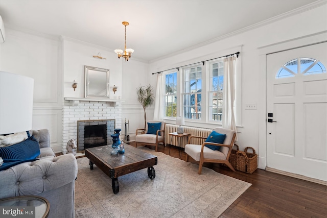 living room with radiator, a brick fireplace, dark hardwood / wood-style floors, ornamental molding, and a notable chandelier