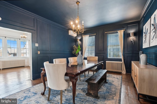 dining space with hardwood / wood-style floors, ornamental molding, radiator, and a chandelier