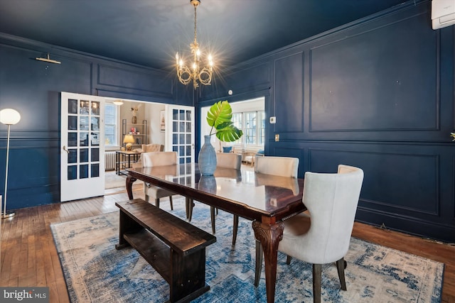 dining space featuring french doors, dark wood-type flooring, an inviting chandelier, a wall unit AC, and crown molding