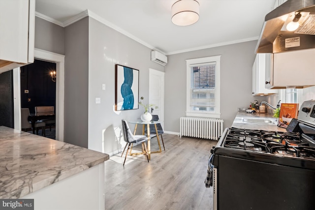 kitchen featuring radiator, white cabinetry, sink, stainless steel range with gas cooktop, and a wall unit AC