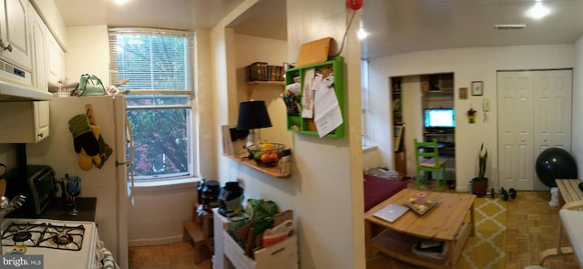 kitchen with white cabinetry, parquet flooring, a healthy amount of sunlight, and gas range gas stove