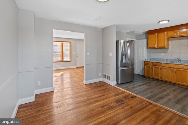 kitchen featuring light stone countertops, tasteful backsplash, dark wood-type flooring, sink, and stainless steel fridge with ice dispenser