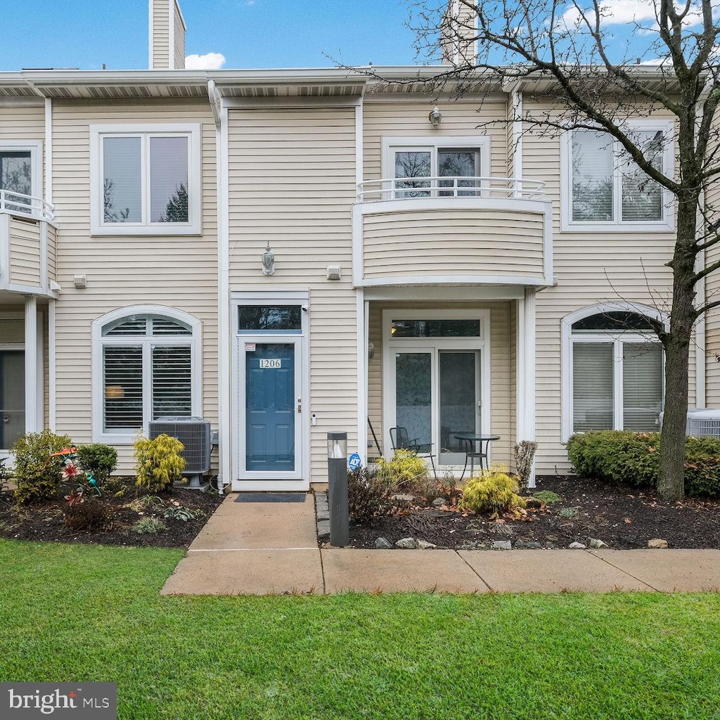 view of property with central AC, a balcony, and a front lawn