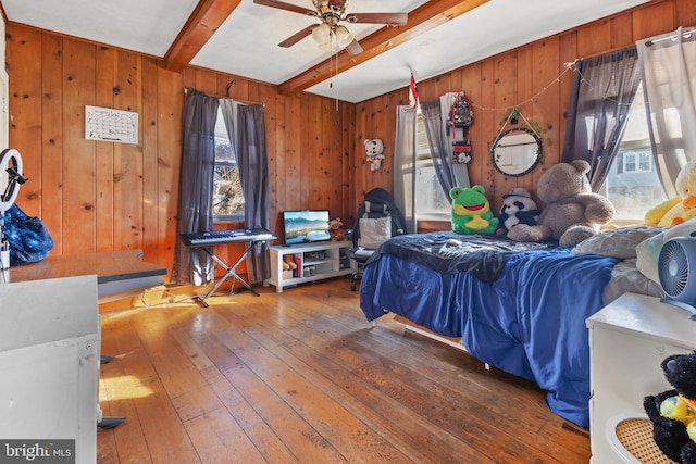 bedroom with multiple windows, wood walls, hardwood / wood-style floors, and beamed ceiling