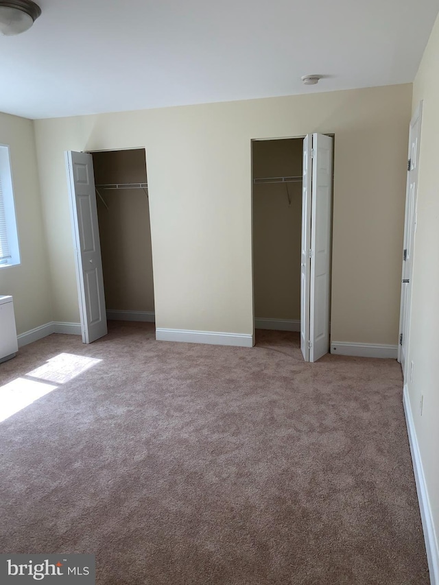 unfurnished bedroom with light colored carpet and two closets