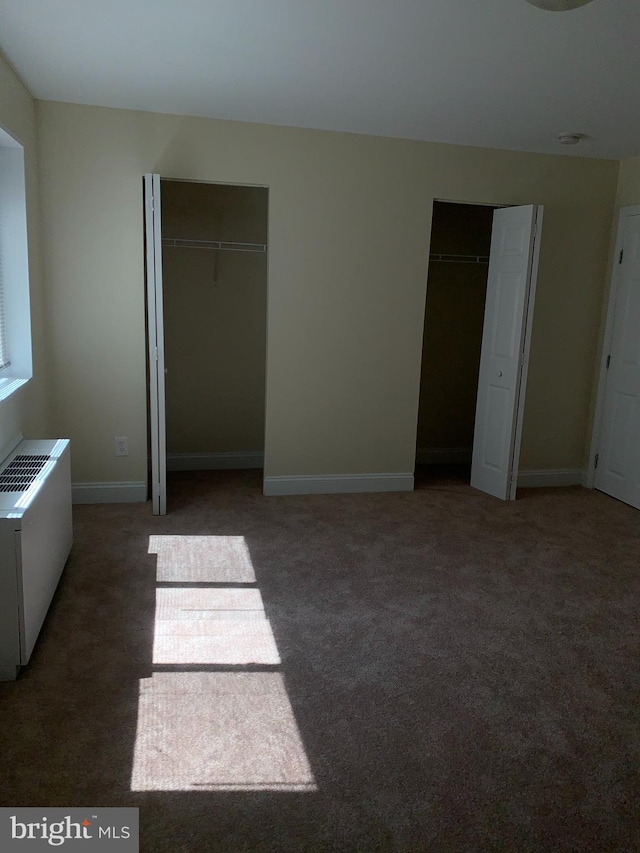 unfurnished bedroom with dark carpet and two closets