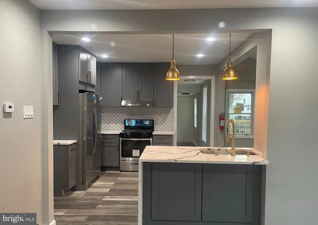 kitchen with dark wood-type flooring, sink, hanging light fixtures, light stone countertops, and stainless steel appliances