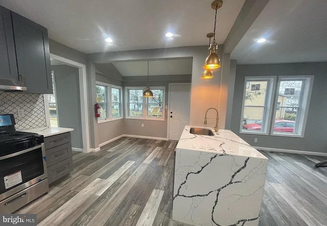 kitchen with light stone counters, a healthy amount of sunlight, sink, stainless steel stove, and hanging light fixtures