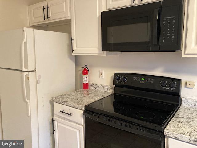 kitchen featuring white cabinets, light stone counters, and black appliances