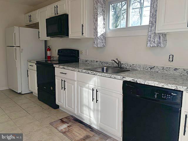 kitchen with light stone counters, sink, white cabinets, and black appliances