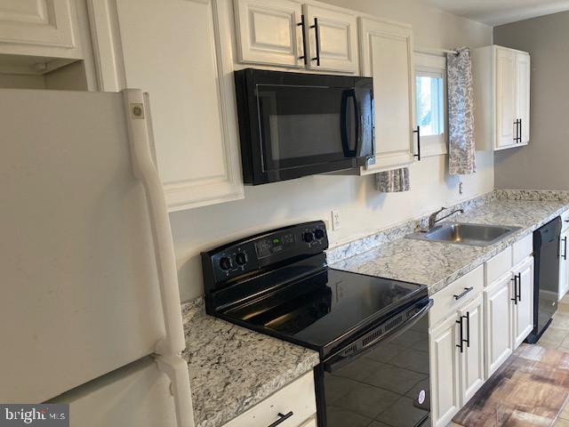 kitchen with white cabinets, sink, light stone countertops, and black appliances