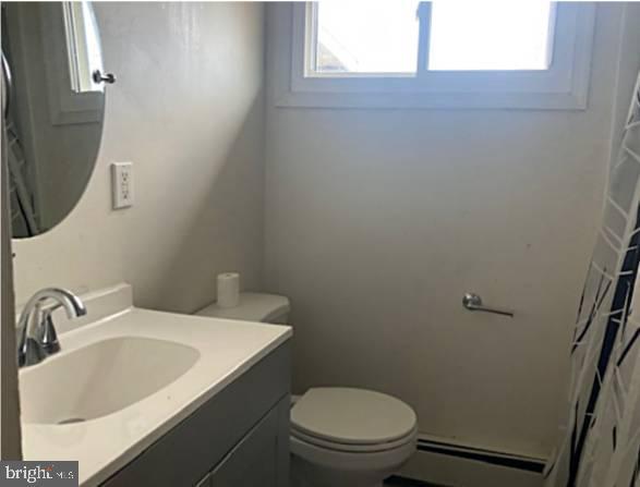 bathroom featuring vanity, curtained shower, toilet, and a baseboard radiator