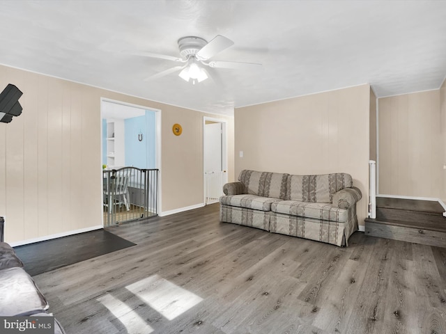 living room featuring ceiling fan, light wood-type flooring, and wooden walls