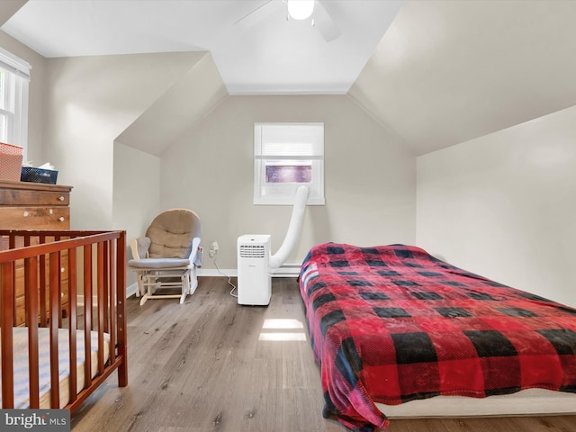 bedroom with multiple windows, ceiling fan, wood-type flooring, and vaulted ceiling