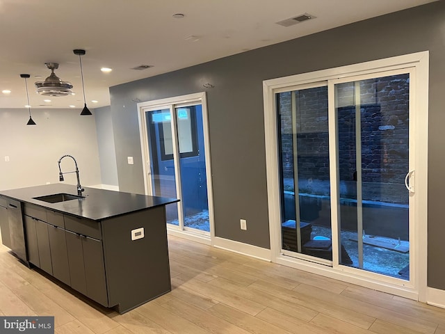 kitchen featuring sink, dishwasher, light wood-type flooring, a center island with sink, and pendant lighting