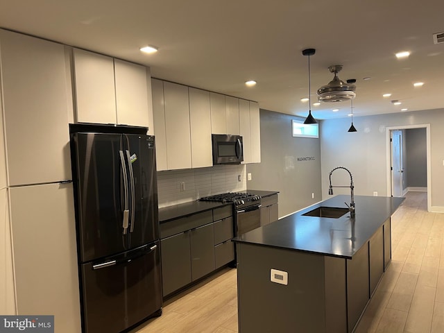 kitchen featuring a center island with sink, stainless steel refrigerator, pendant lighting, sink, and white cabinetry