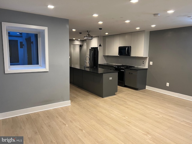 kitchen with sink, an island with sink, decorative backsplash, hanging light fixtures, and black appliances