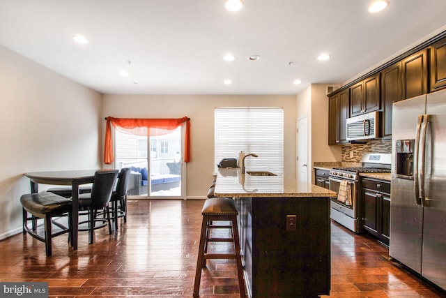 kitchen featuring decorative backsplash, a kitchen breakfast bar, dark hardwood / wood-style flooring, stainless steel appliances, and an island with sink