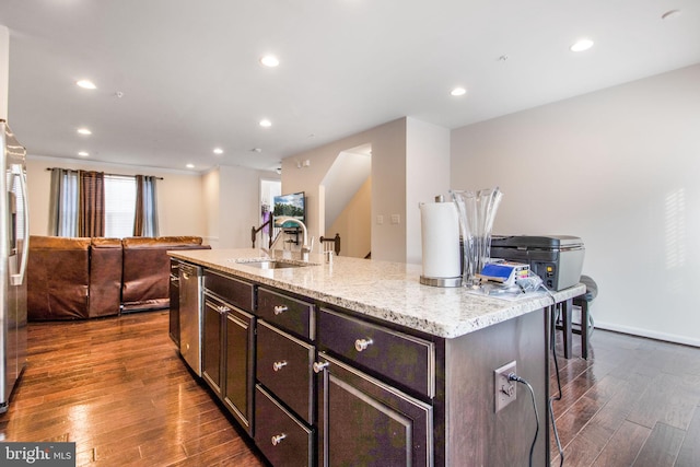 kitchen with a kitchen island with sink, a kitchen breakfast bar, sink, light stone counters, and dark hardwood / wood-style flooring