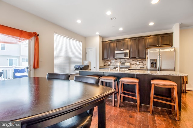 kitchen with tasteful backsplash, a breakfast bar, stainless steel appliances, sink, and a large island with sink