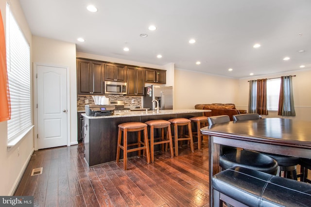 kitchen featuring decorative backsplash, a breakfast bar, appliances with stainless steel finishes, and dark wood-type flooring