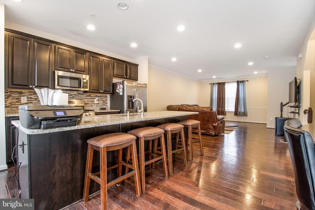 kitchen featuring dark brown cabinets, stainless steel appliances, light stone counters, and a breakfast bar area