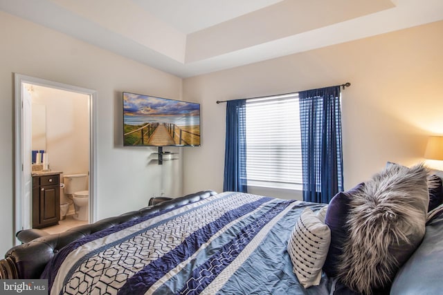 bedroom featuring ensuite bathroom and a raised ceiling