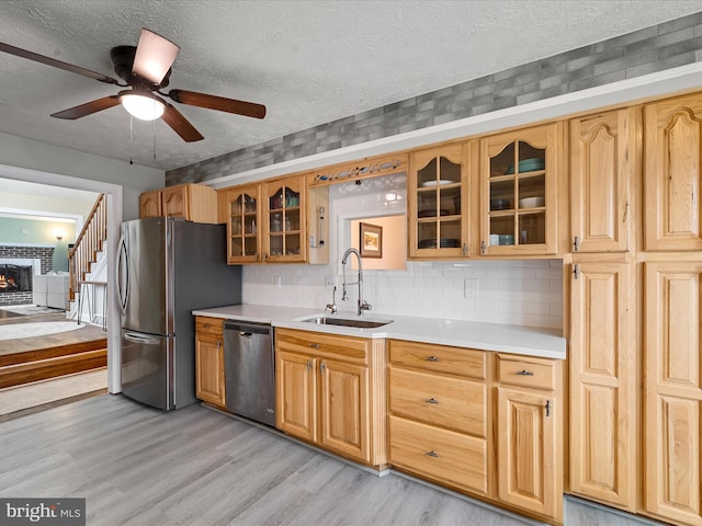 kitchen with ceiling fan, sink, stainless steel appliances, a textured ceiling, and light wood-type flooring