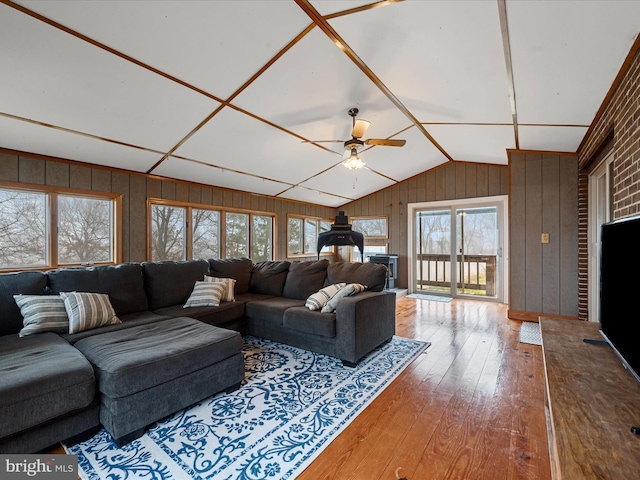 living room with ceiling fan, wood-type flooring, wooden walls, and vaulted ceiling