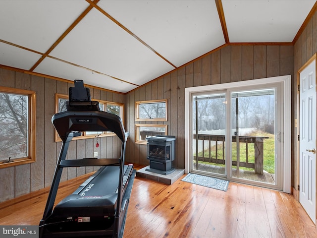 exercise area featuring plenty of natural light, a wood stove, wooden walls, and lofted ceiling