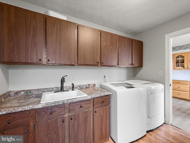 clothes washing area with cabinets, light wood-type flooring, a textured ceiling, sink, and independent washer and dryer