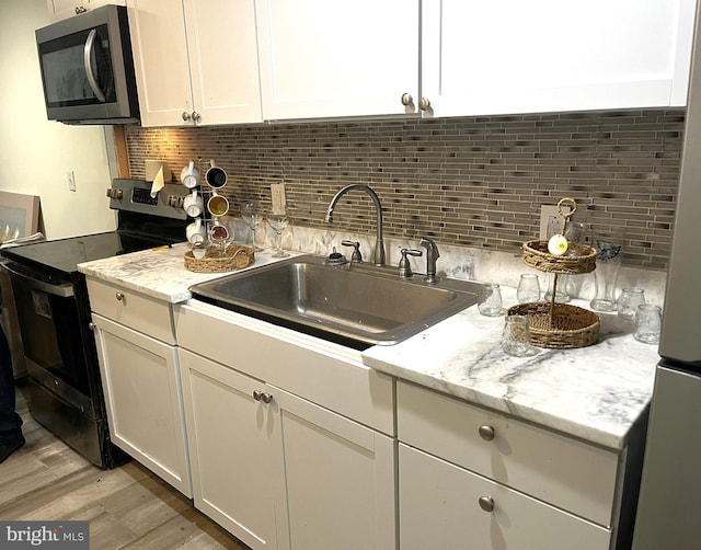 kitchen with light stone countertops, tasteful backsplash, sink, light hardwood / wood-style floors, and black / electric stove