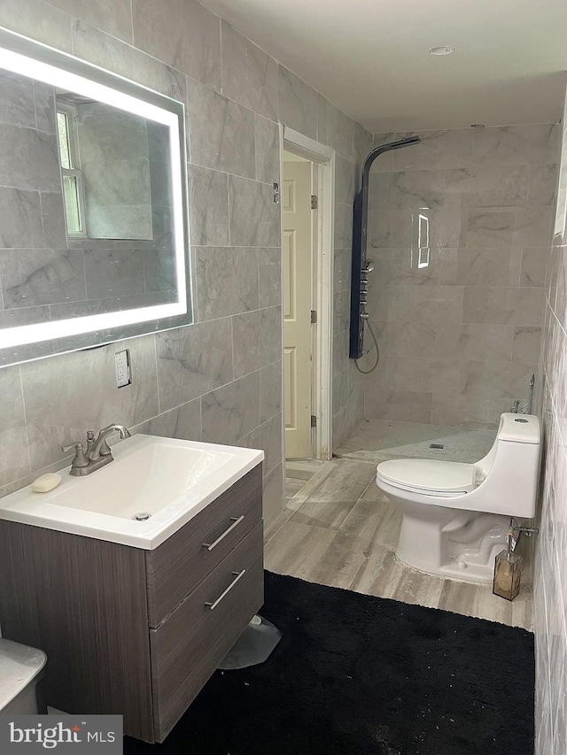 bathroom featuring a tile shower, vanity, wood-type flooring, and tile walls