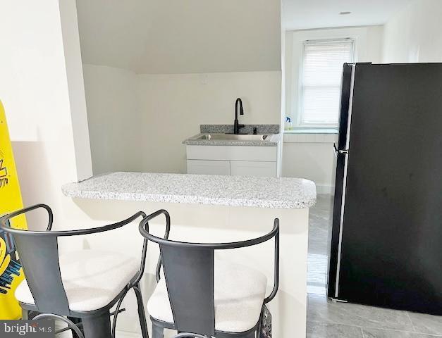 kitchen with white cabinets, black refrigerator, and sink