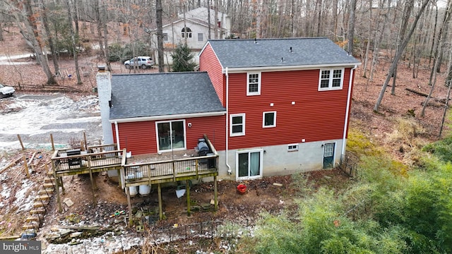 rear view of house featuring a chimney, a deck, and roof with shingles