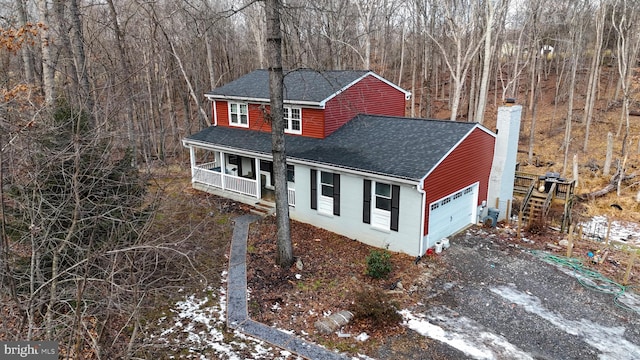 view of front of house with an attached garage, roof with shingles, covered porch, and a chimney