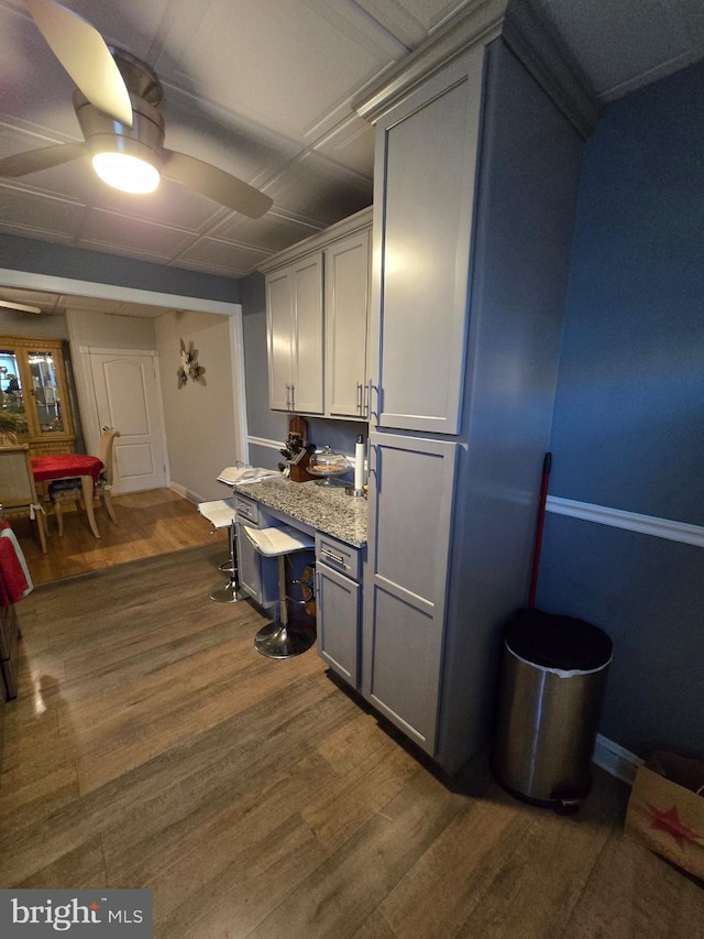 kitchen featuring gray cabinetry, light stone counters, ceiling fan, and dark wood-type flooring