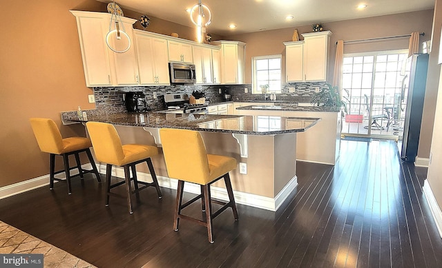 kitchen with white cabinets, appliances with stainless steel finishes, decorative light fixtures, a kitchen bar, and kitchen peninsula