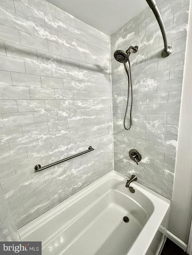 bathroom featuring a textured ceiling and tiled shower / bath