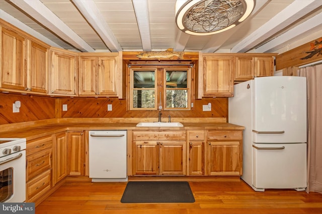 kitchen with wood walls, white appliances, sink, light hardwood / wood-style flooring, and beam ceiling