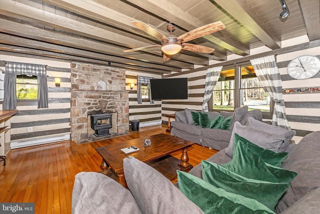 living room featuring a wood stove, hardwood / wood-style flooring, ceiling fan, a baseboard radiator, and beamed ceiling