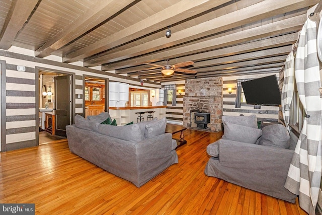 living room featuring beam ceiling, hardwood / wood-style flooring, a wood stove, and ceiling fan