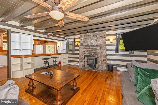 living room featuring hardwood / wood-style flooring, ceiling fan, a wood stove, and beamed ceiling