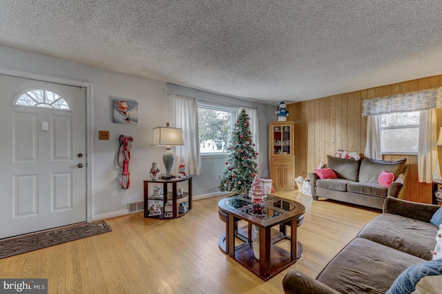 living room featuring a textured ceiling, wooden walls, and light hardwood / wood-style flooring