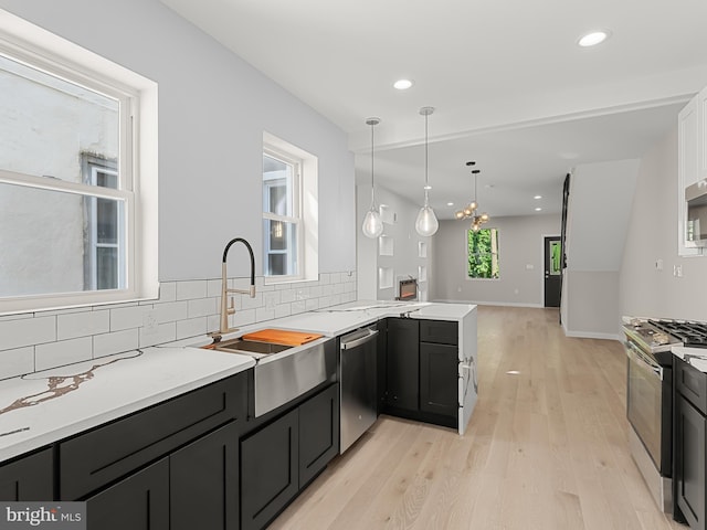 kitchen with light hardwood / wood-style flooring, appliances with stainless steel finishes, tasteful backsplash, decorative light fixtures, and kitchen peninsula