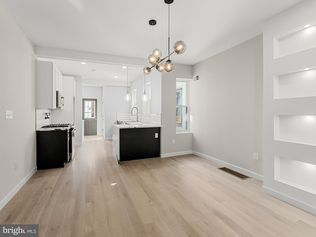 kitchen with white gas stove, an inviting chandelier, light hardwood / wood-style floors, decorative light fixtures, and white cabinets