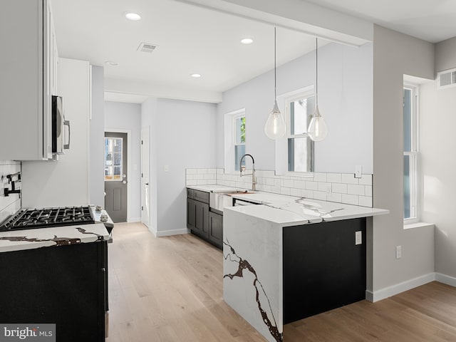 kitchen with light stone counters, backsplash, hanging light fixtures, and light hardwood / wood-style flooring