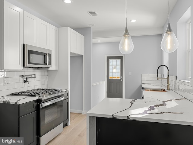 kitchen with stainless steel appliances, sink, decorative light fixtures, light hardwood / wood-style flooring, and white cabinetry