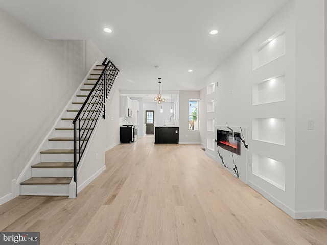 unfurnished living room with a notable chandelier, light hardwood / wood-style floors, and sink